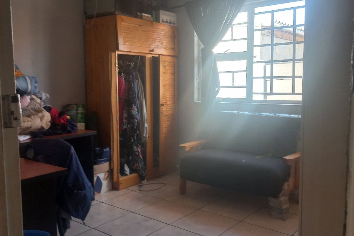 A bedroom featuring tiled flooring and a window with security bars, offering a functional space that could benefit from cosmetic updates.