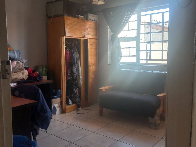 A bedroom featuring tiled flooring and a window with security bars, offering a functional space that could benefit from cosmetic updates.