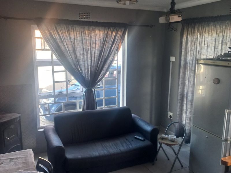 A living area featuring tiled flooring, a ceiling-mounted projector, and natural light through windows with security bars.