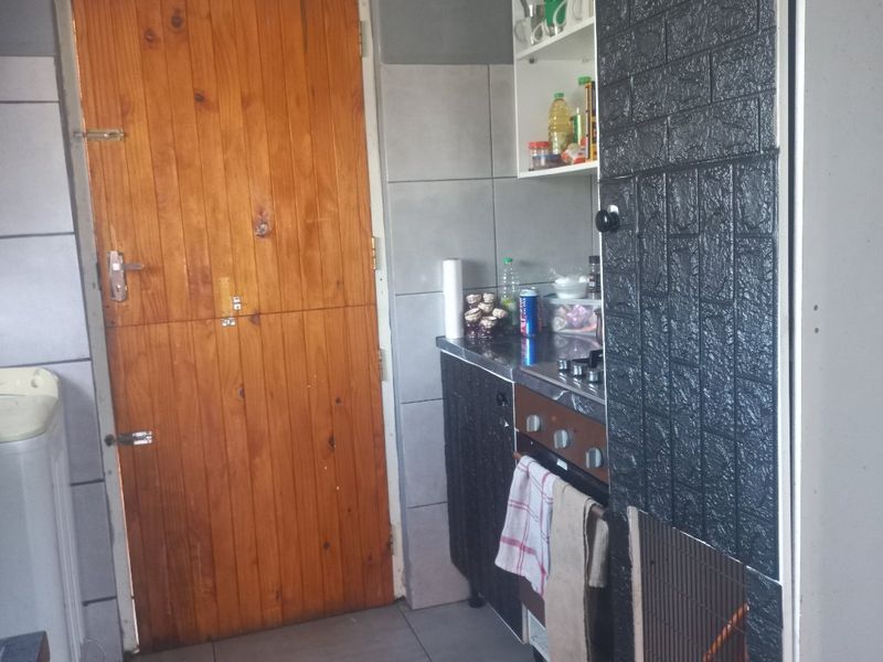 A compact kitchen area featuring tiled floors, wall tiling, and built-in cooking appliances, with a wooden door leading to the exterior.