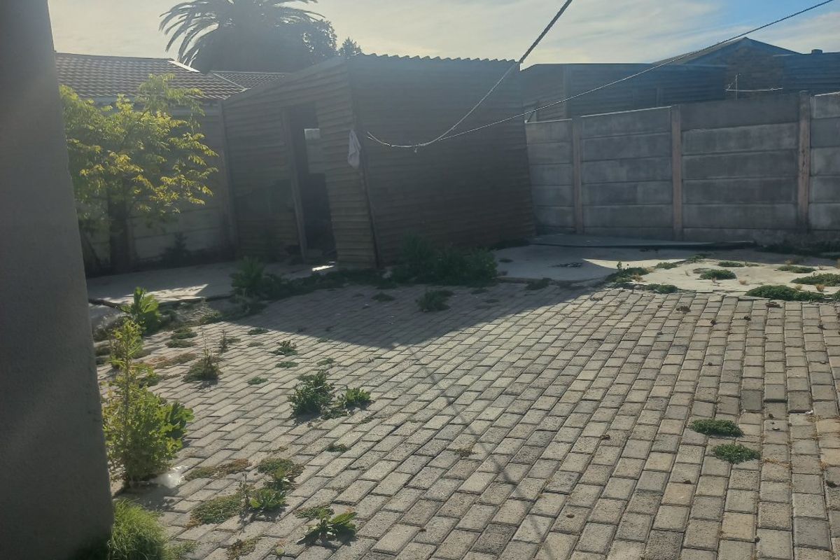 Rear garden area featuring paved patio, precast boundary walling, and a timber storage shed, requiring maintenance and landscaping.