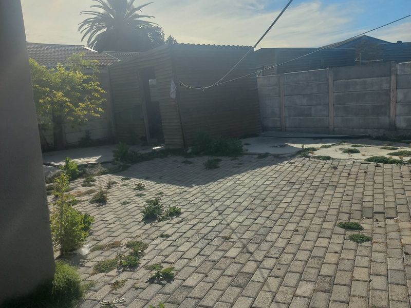 Rear garden area featuring paved patio, precast boundary walling, and a timber storage shed, requiring maintenance and landscaping.
