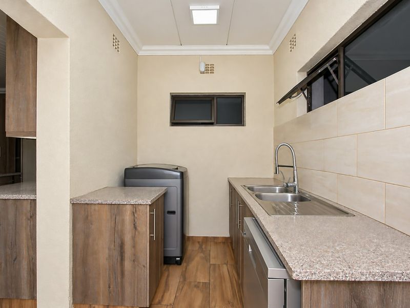 A well-maintained laundry room featuring modern built-in cabinetry, laminate countertops, a double stainless steel sink, and tiled flooring.
