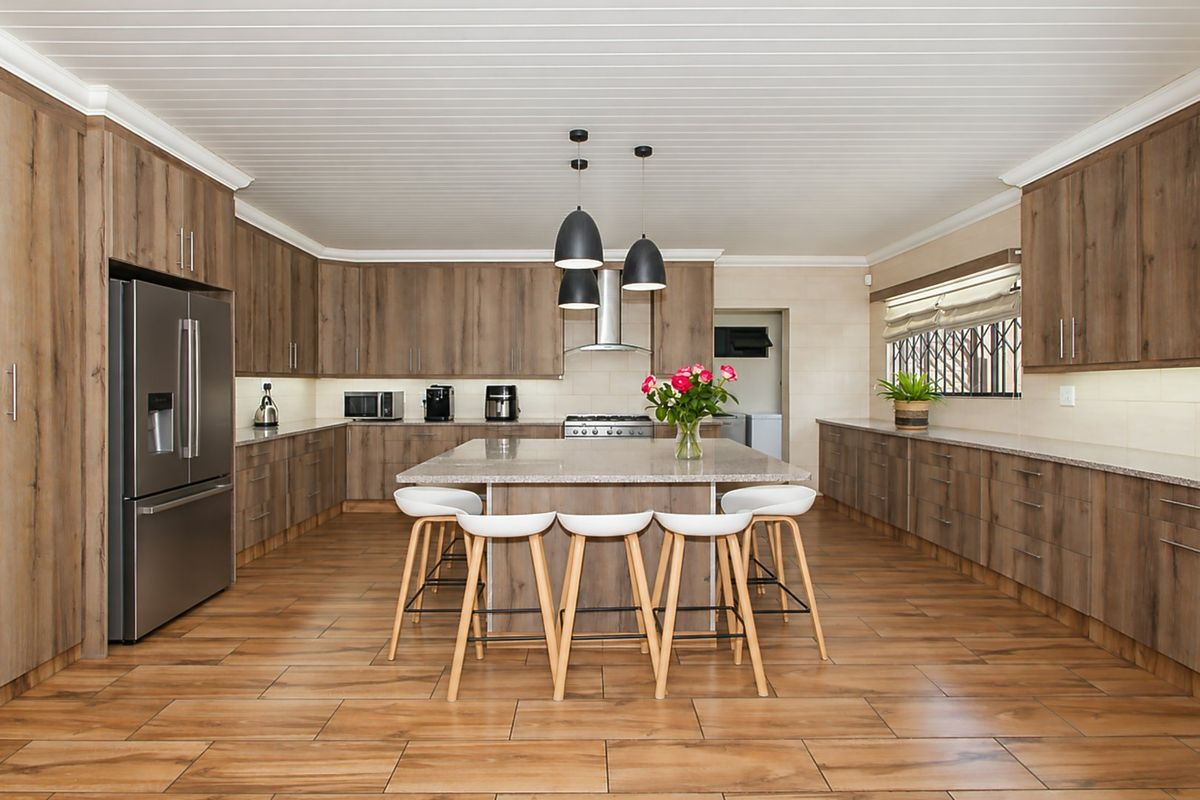Spacious modern kitchen featuring extensive wood-finish cabinetry, a large central island with stone countertops, integrated appliances, and stylish pendant lighting.