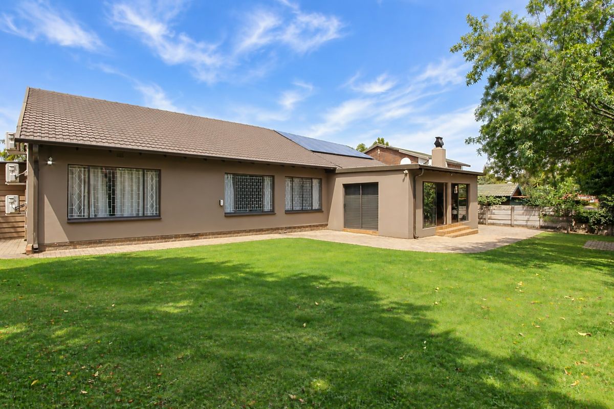 Rear view of the house featuring a paved patio area, well-maintained lawn, solar panels on the roof, and secure window bars.
