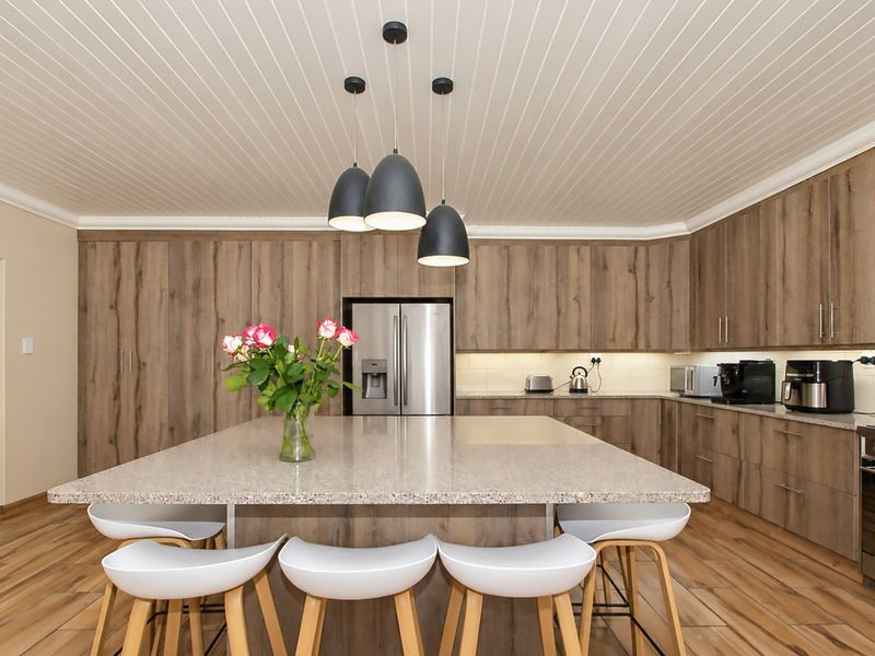Modern kitchen featuring wood-look cabinetry, a large central island with stone countertops, integrated appliances, and stylish pendant lighting.