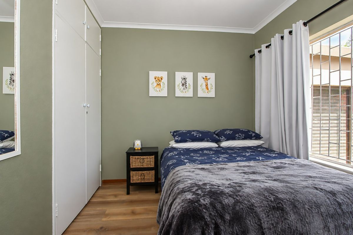 A well-maintained bedroom featuring laminate flooring, a built-in wardrobe, and a window fitted with security bars.