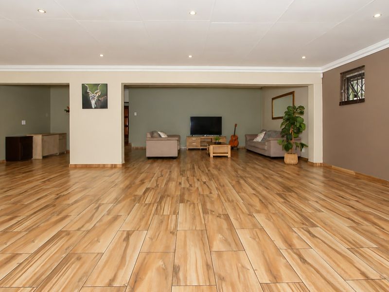 Spacious living area featuring wood-look tile flooring, recessed downlighting, and neutral wall tones, offering a versatile open-plan layout.