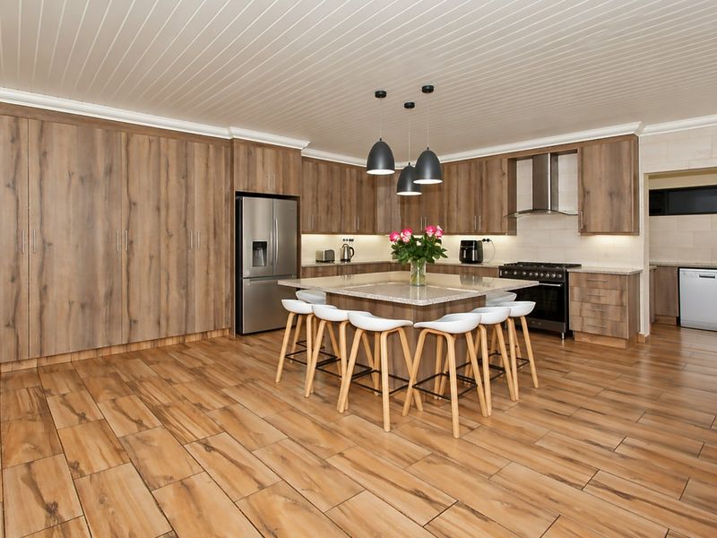Modern kitchen featuring wood-grain cabinetry, a central island with stone countertops, gas stove, and integrated appliances, complemented by stylish pendant lighting and tiled flooring.