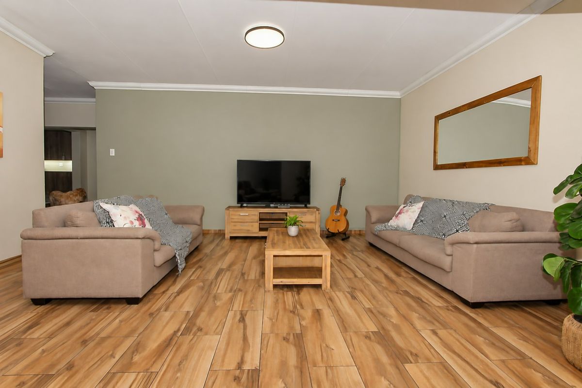 A well-maintained living room featuring wood-look tile flooring, neutral wall tones, and classic cove cornicing, providing a comfortable and functional living space.