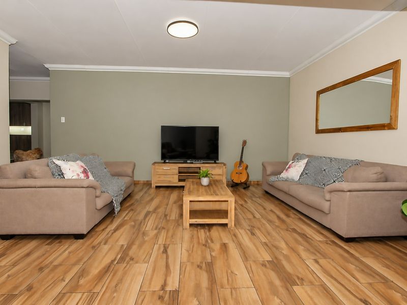 A well-maintained living room featuring wood-look tile flooring, neutral wall tones, and classic cove cornicing, providing a comfortable and functional living space.
