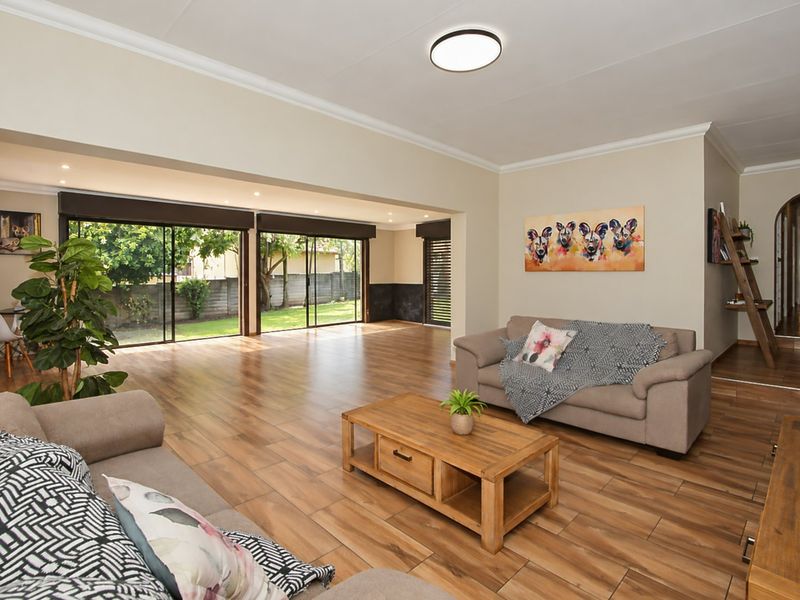 Spacious open-plan living area featuring wood-look tile flooring, recessed lighting, and large sliding glass doors providing seamless access to the rear garden.