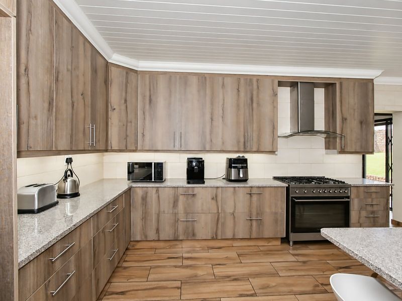 Modern kitchen featuring wood-look cabinetry, granite countertops, a gas stove with extractor fan, and durable plank-style floor tiles.