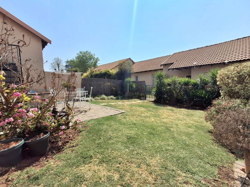 A private rear garden featuring a paved patio area, established lawn, and perimeter reed fencing, providing a functional outdoor space for the townhouse.
