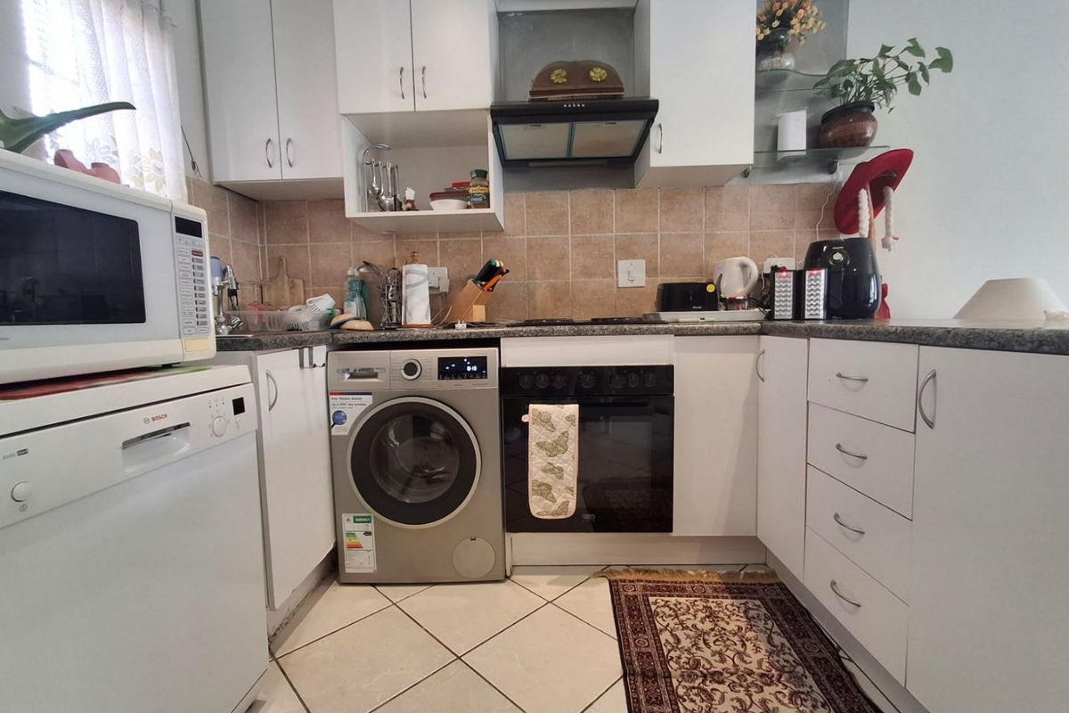 Compact kitchen featuring white cabinetry, stone countertops, tiled backsplash, and integrated oven with extractor fan.