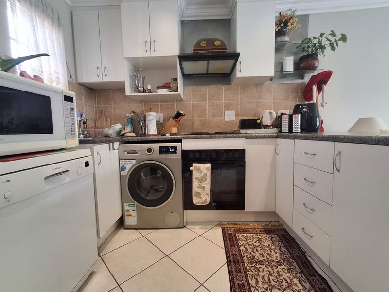 Compact kitchen featuring white cabinetry, stone countertops, tiled backsplash, and integrated oven with extractor fan.