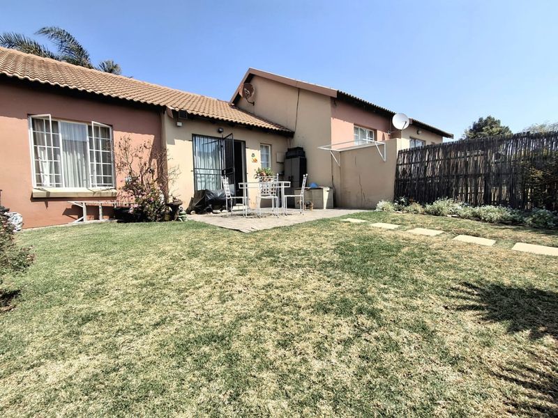 Rear view of the townhouse featuring a paved patio area, private garden with lawn, and secure access points.