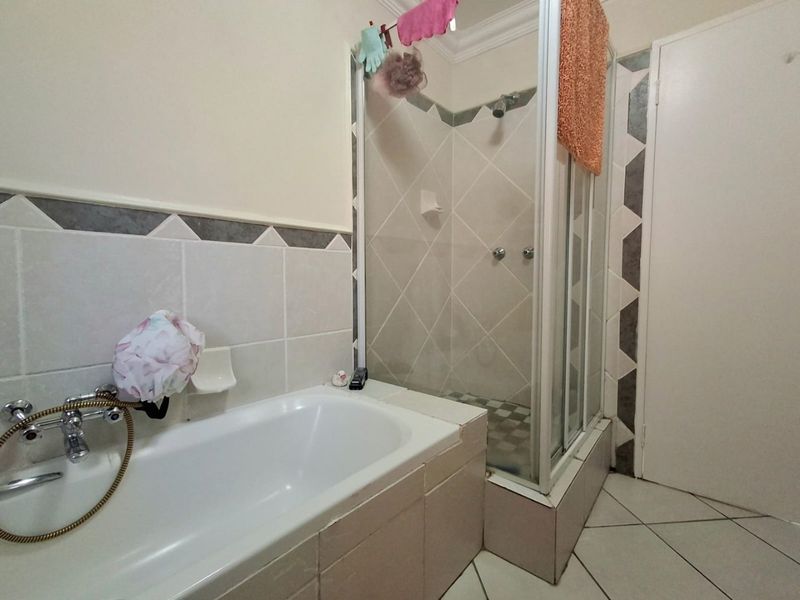 A functional bathroom featuring a built-in bathtub and a separate shower enclosure with tiled finishes throughout.