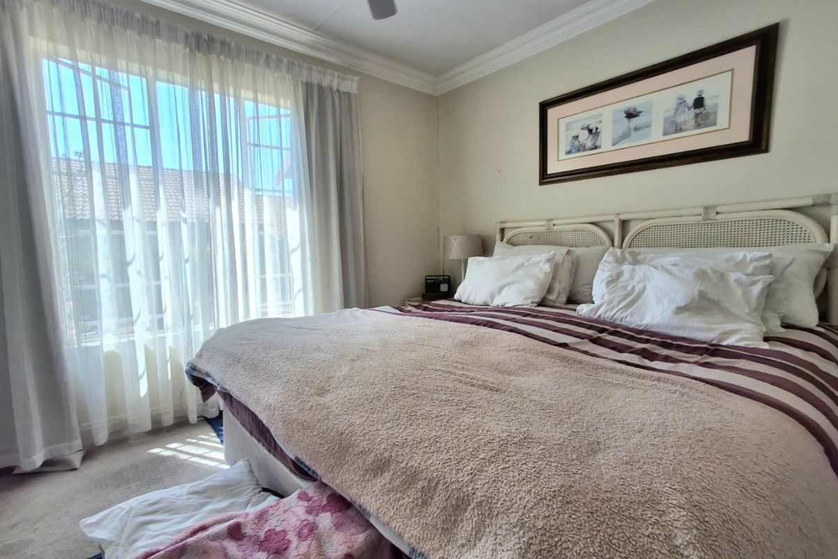 A well-lit bedroom featuring a ceiling fan, decorative cornice, and large window with security gate, offering a comfortable and functional living space.