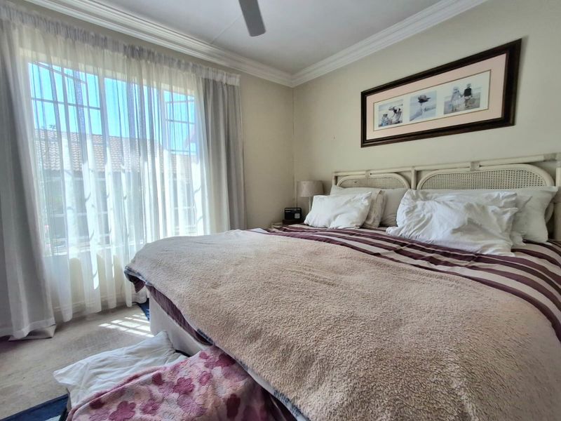A well-lit bedroom featuring a ceiling fan, decorative cornice, and large window with security gate, offering a comfortable and functional living space.