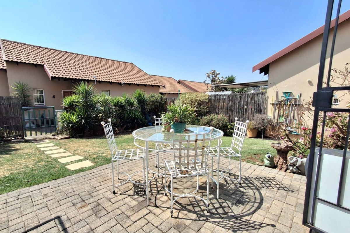 A private rear garden featuring a paved patio area, established lawn, and perimeter reed fencing, providing a pleasant outdoor space for relaxation.