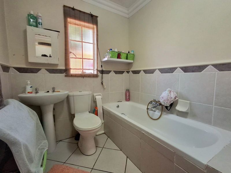 A functional bathroom featuring a pedestal basin, toilet, and bathtub with tiled walls and flooring, offering a classic layout ready for modern updates.