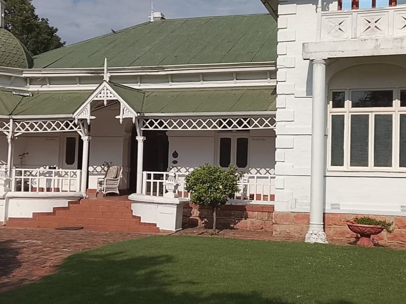 A historic commercial property featuring a classic veranda with decorative timber fretwork, stone foundation, and a distinctive cupola roof design.