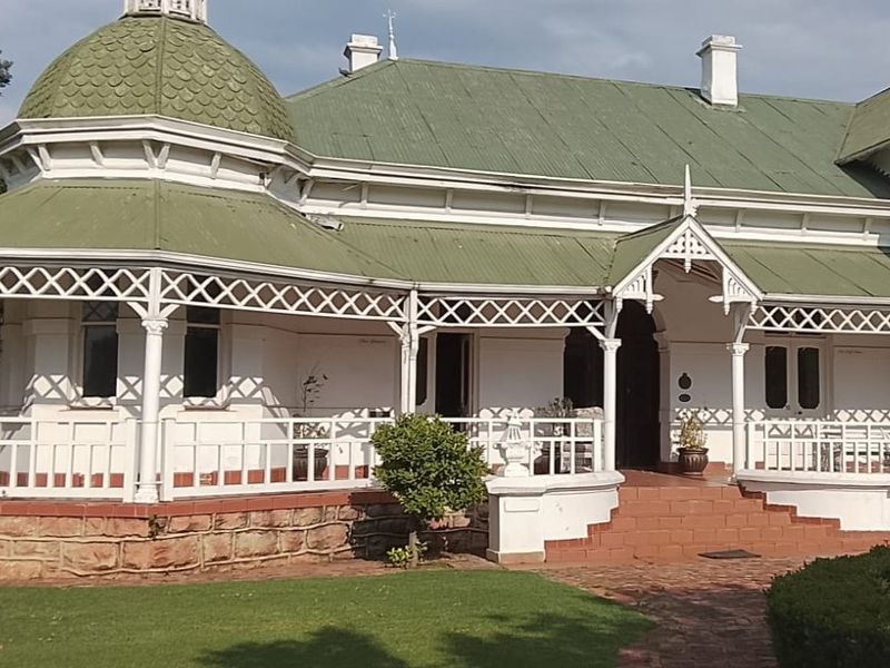 A charming historic commercial property featuring a distinctive domed roof, wrap-around timber lattice veranda, and classic stone masonry base with well-maintained garden surroundings.