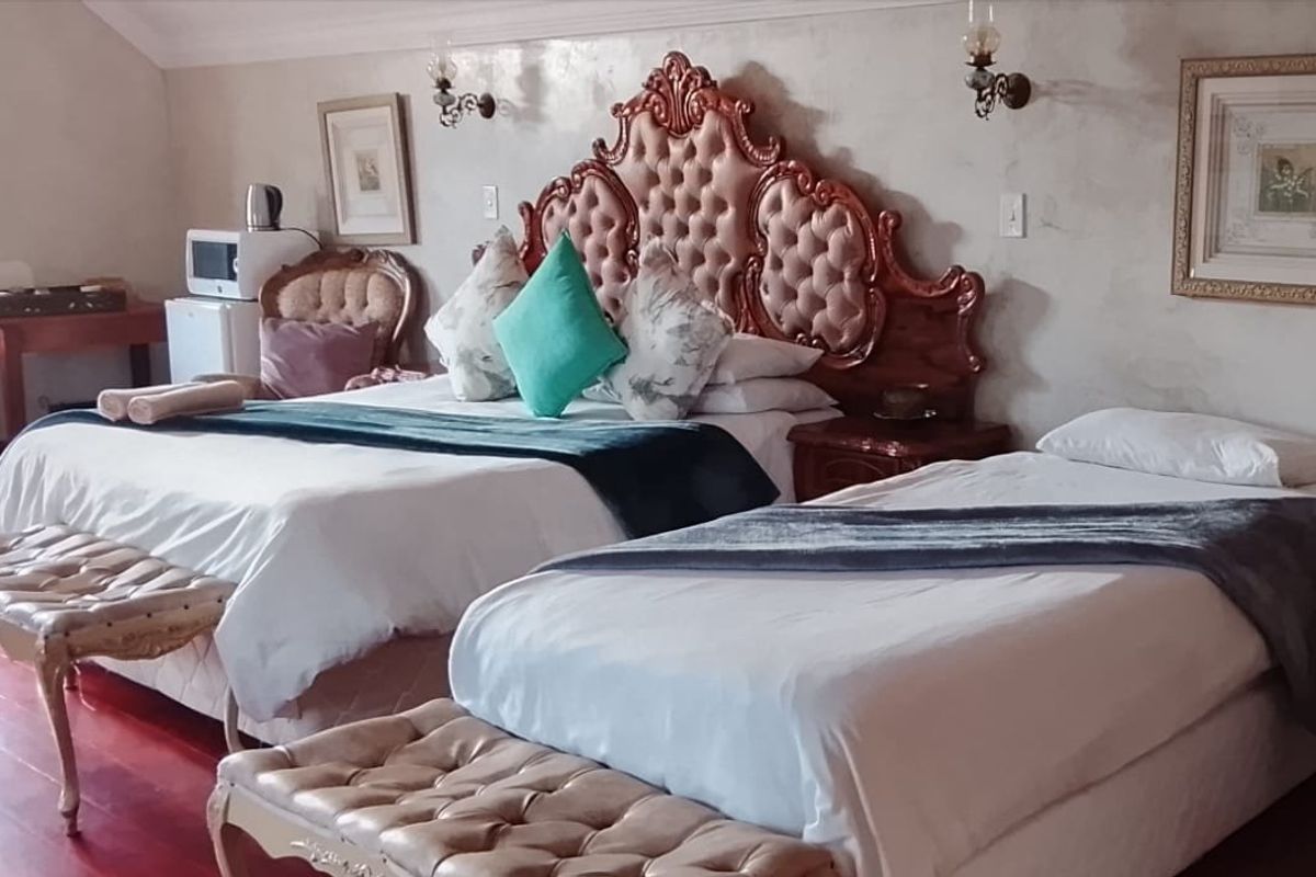 A spacious bedroom featuring hardwood flooring and wall-mounted lighting fixtures, currently furnished with multiple beds.