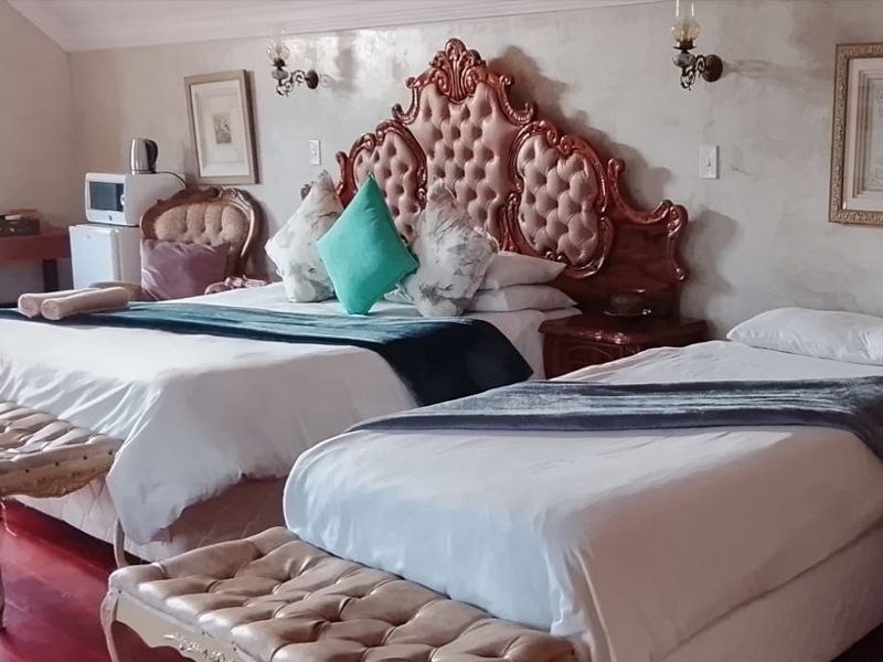 A spacious bedroom featuring hardwood flooring and wall-mounted lighting fixtures, currently furnished with multiple beds.