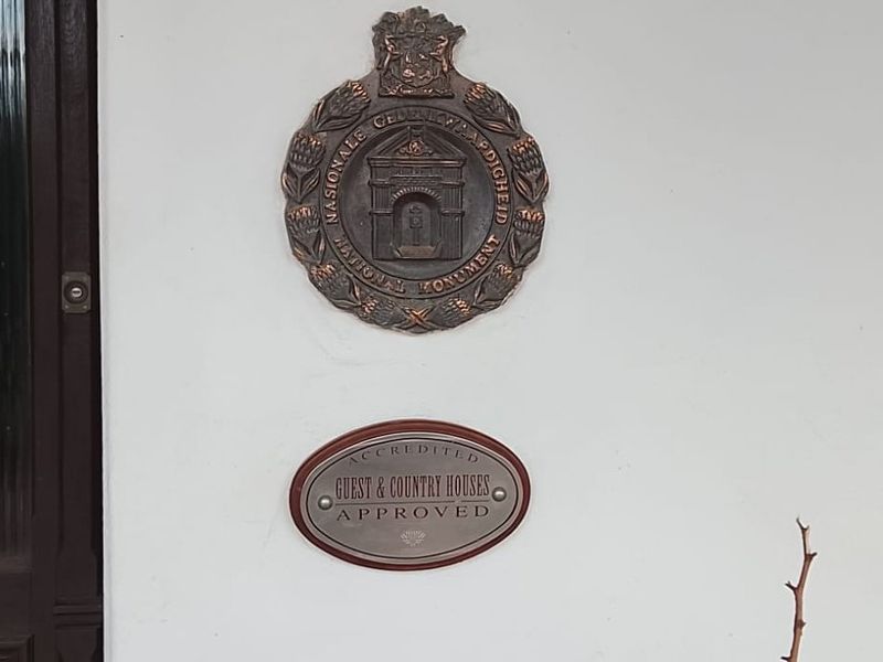 A close-up view of the building exterior featuring a national monument plaque and guest house accreditation signage mounted on the wall.