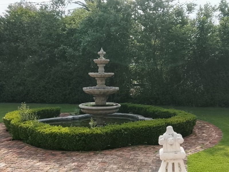 A well-maintained garden area featuring a tiered stone fountain surrounded by manicured hedging and classic brick paving.