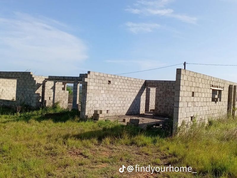An unfinished residential structure featuring exposed concrete block walls set on a rural farm property.