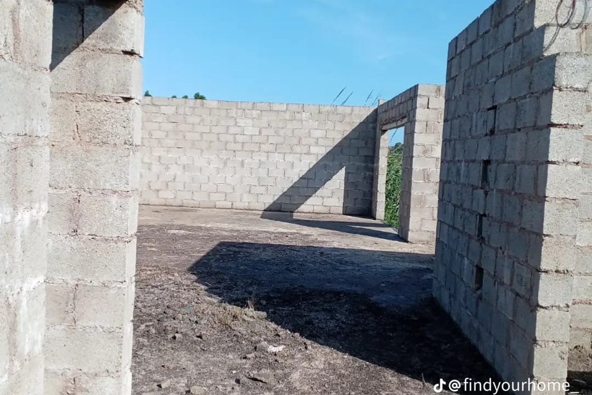 An unfinished construction site showing exposed concrete block walls and a dirt floor, representing the early stages of property development.