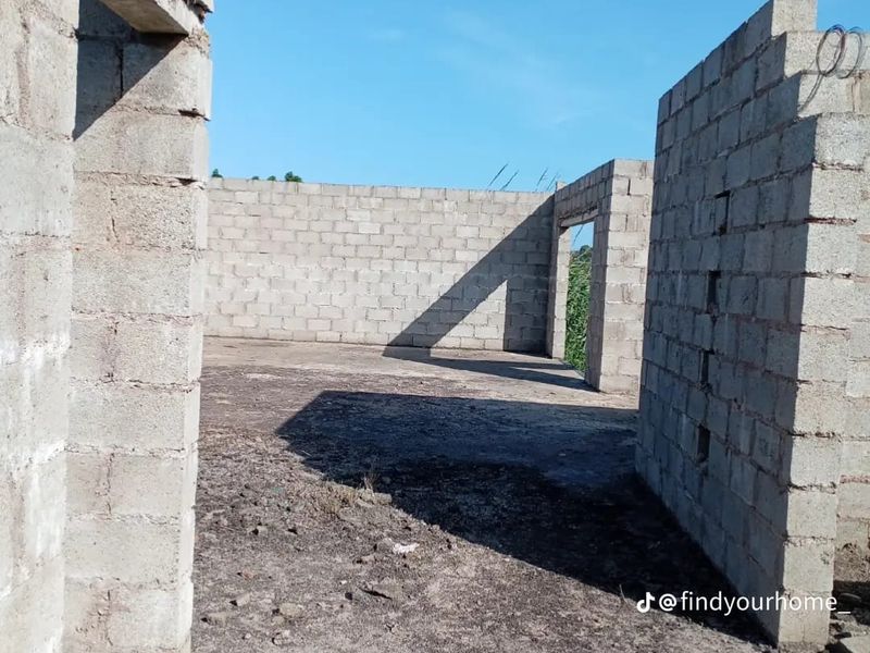 An unfinished construction site showing exposed concrete block walls and a dirt floor, representing the early stages of property development.