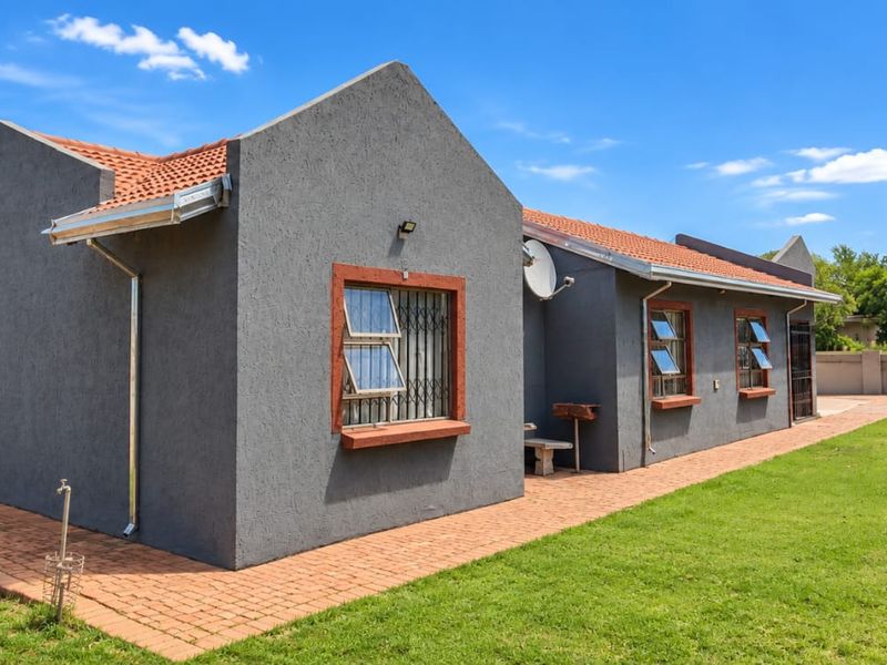 Rear view of the house featuring a grey textured facade, terracotta roof tiles, a brick paved walkway, and a well-maintained garden area.