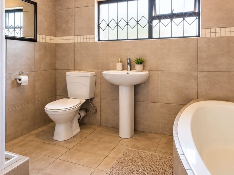 A well-maintained bathroom featuring a pedestal basin, toilet, shower enclosure, and a built-in bathtub with neutral wall and floor tiling.