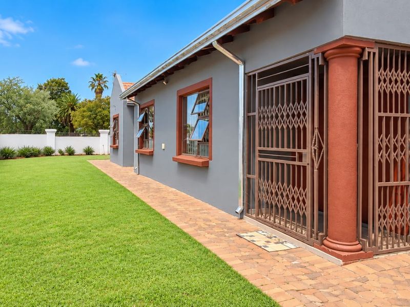 A well-maintained rear exterior featuring a paved walkway, manicured lawn, secure metal gate, and glass block detailing along the side of the house.