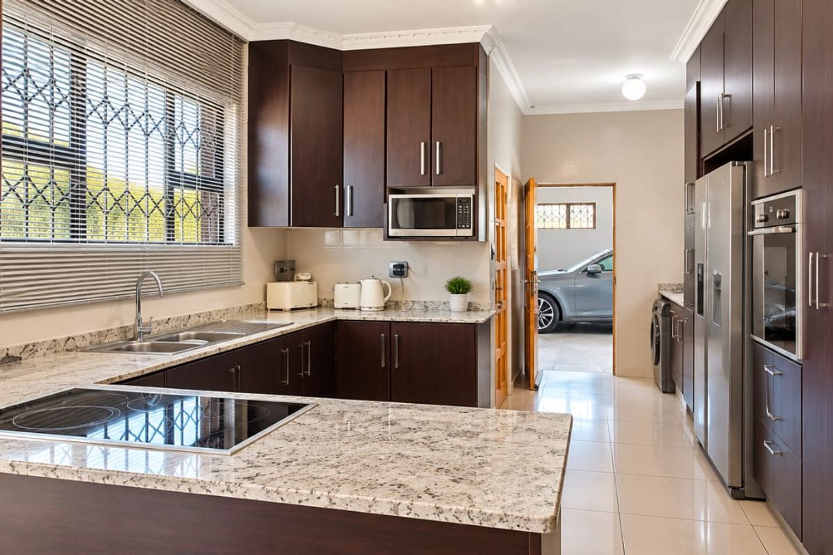 Modern kitchen featuring dark wood cabinetry, granite countertops, built-in oven, and electric hob, with tiled flooring and direct access to the garage area.