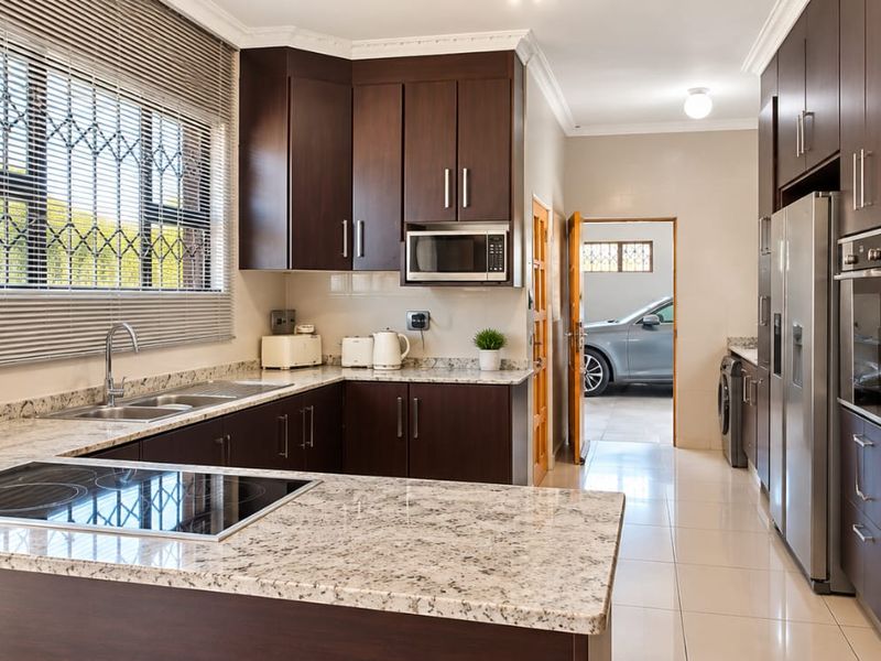 Modern kitchen featuring dark wood cabinetry, granite countertops, built-in oven, and electric hob, with tiled flooring and direct access to the garage area.