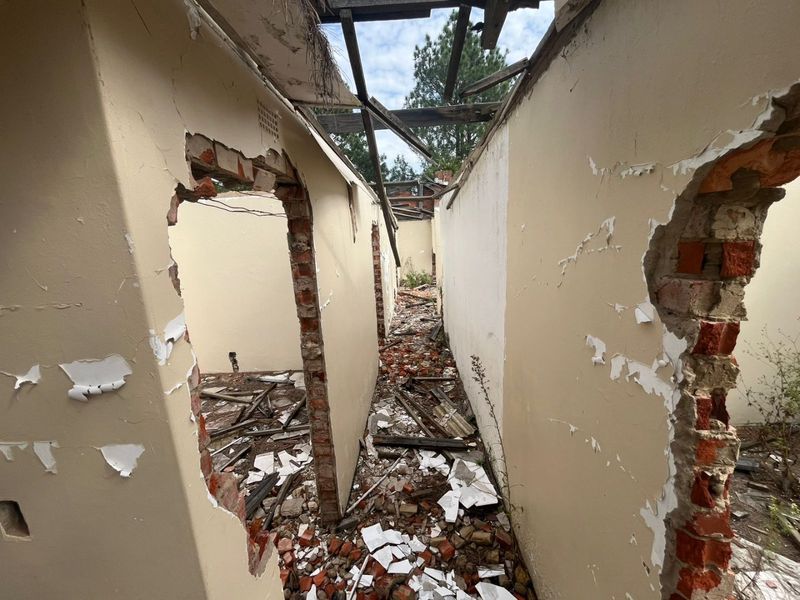 A severely dilapidated interior space showing significant structural damage, including a collapsed roof and crumbling wall finishes.