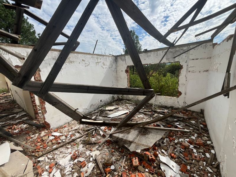 A severely dilapidated structure showing significant structural failure, collapsed roof timbers, and extensive debris within the interior space.