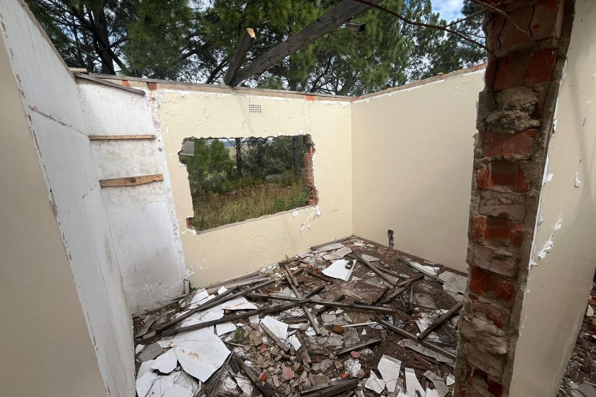 A severely dilapidated room structure with missing roof, damaged walls, and significant debris, requiring extensive renovation or demolition.