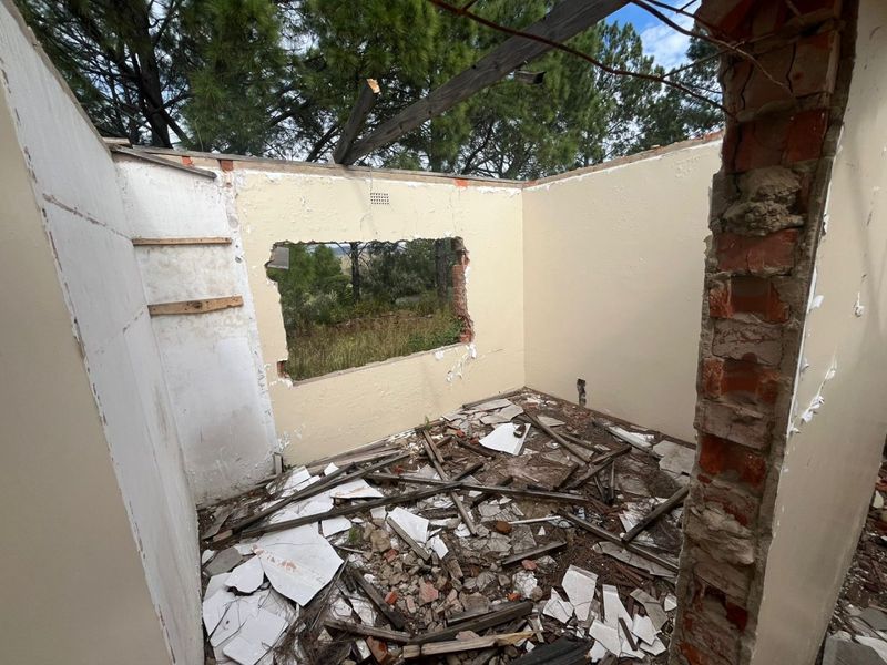 A severely dilapidated room structure with missing roof, damaged walls, and significant debris, requiring extensive renovation or demolition.