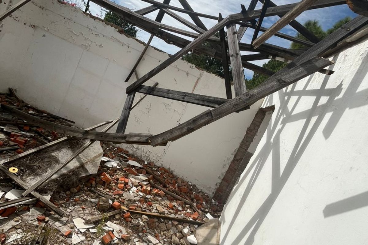 A severely damaged structure showing a collapsed roof and significant debris, indicating a state of total disrepair requiring major reconstruction.