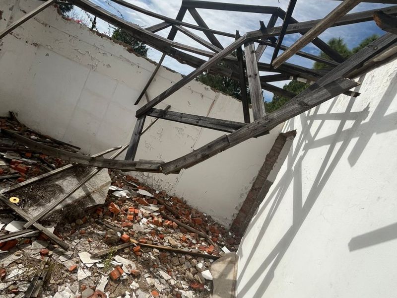 A severely damaged structure showing a collapsed roof and significant debris, indicating a state of total disrepair requiring major reconstruction.