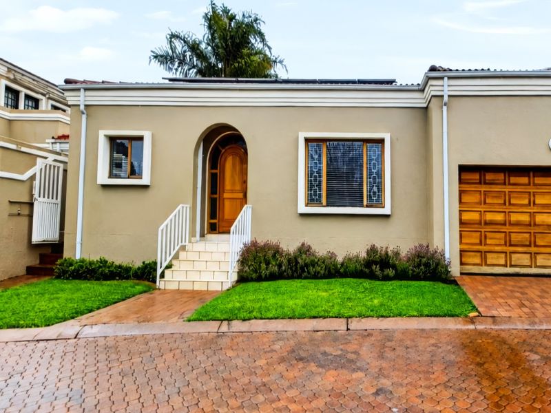 Front elevation of a well-maintained house featuring a paved driveway, landscaped lawn, arched wooden entrance door, and a wooden sectional garage door.