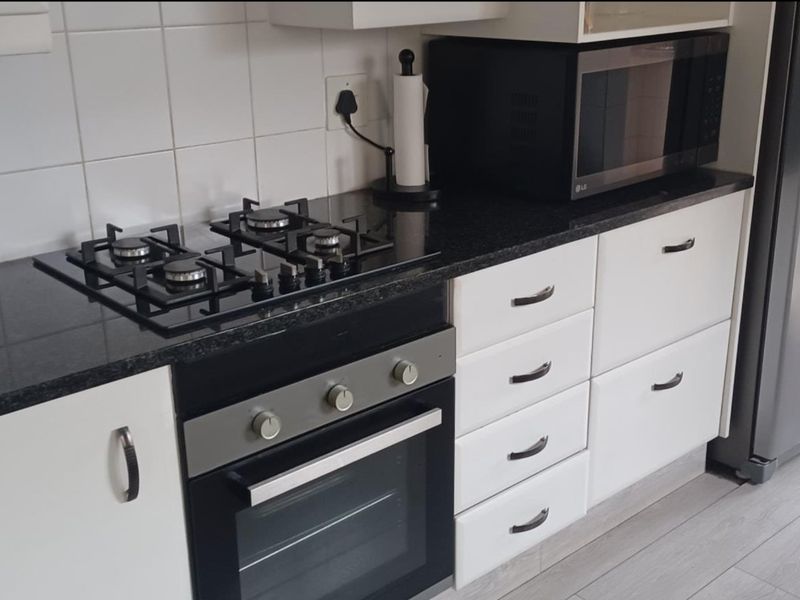 A functional kitchen featuring white cabinetry, granite countertops, a gas hob, and a built-in oven with a tiled backsplash.