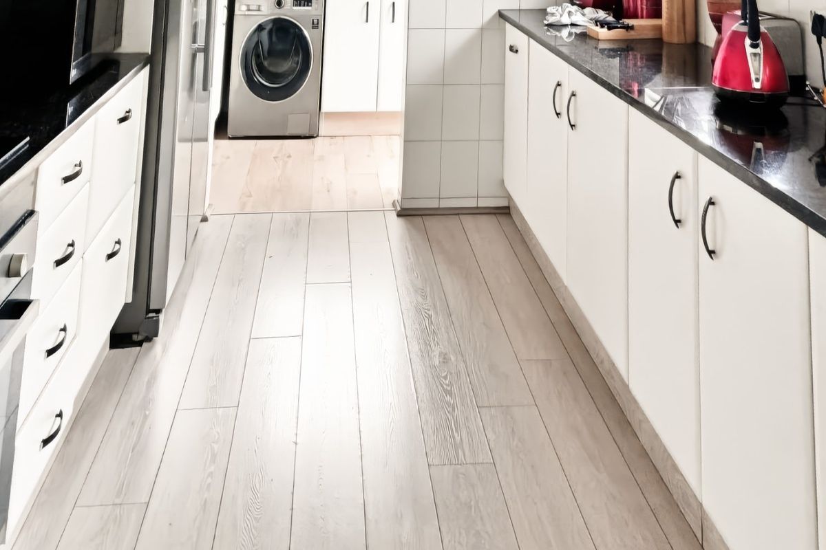 A functional kitchen featuring white cabinetry, dark granite countertops, tiled splashbacks, and light-toned laminate flooring, with an integrated oven and hob.