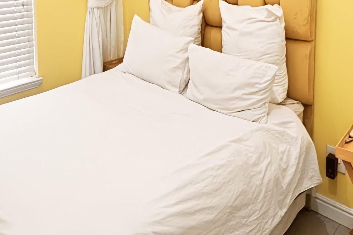 A cozy bedroom featuring yellow walls, white venetian blinds, and neutral flooring, providing a bright and functional sleeping space.